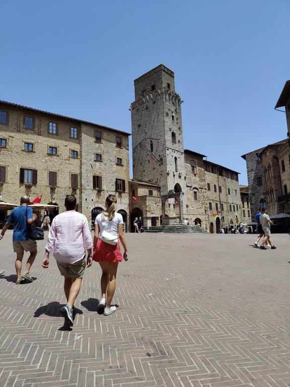 couple crossing central square medieval town towards water well and tower